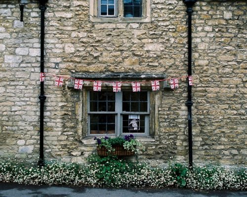 Rustic stone facade of a traditional British house with flag bunting and flowers.